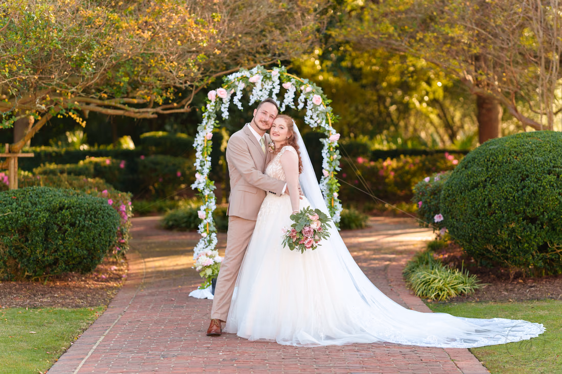 The bride and groom cheek to cheek under the flower arch at Pine Lakes Country Club