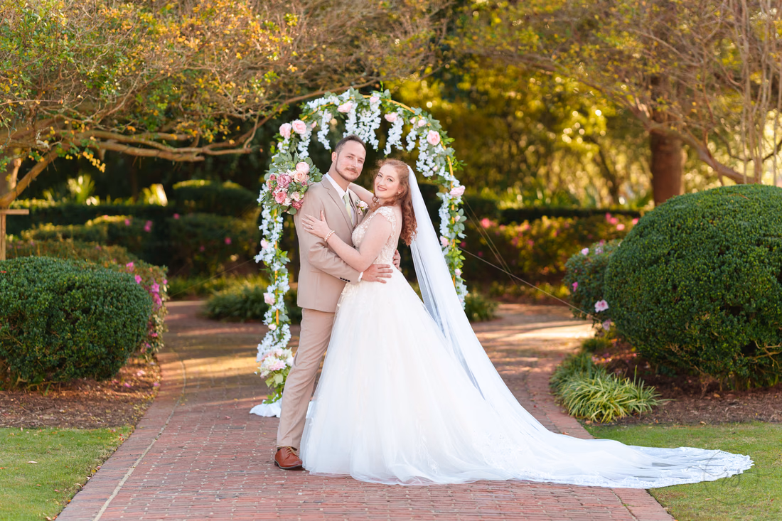 The bride and groom hug and smile under the flower arch at Pine Lakes Country Club