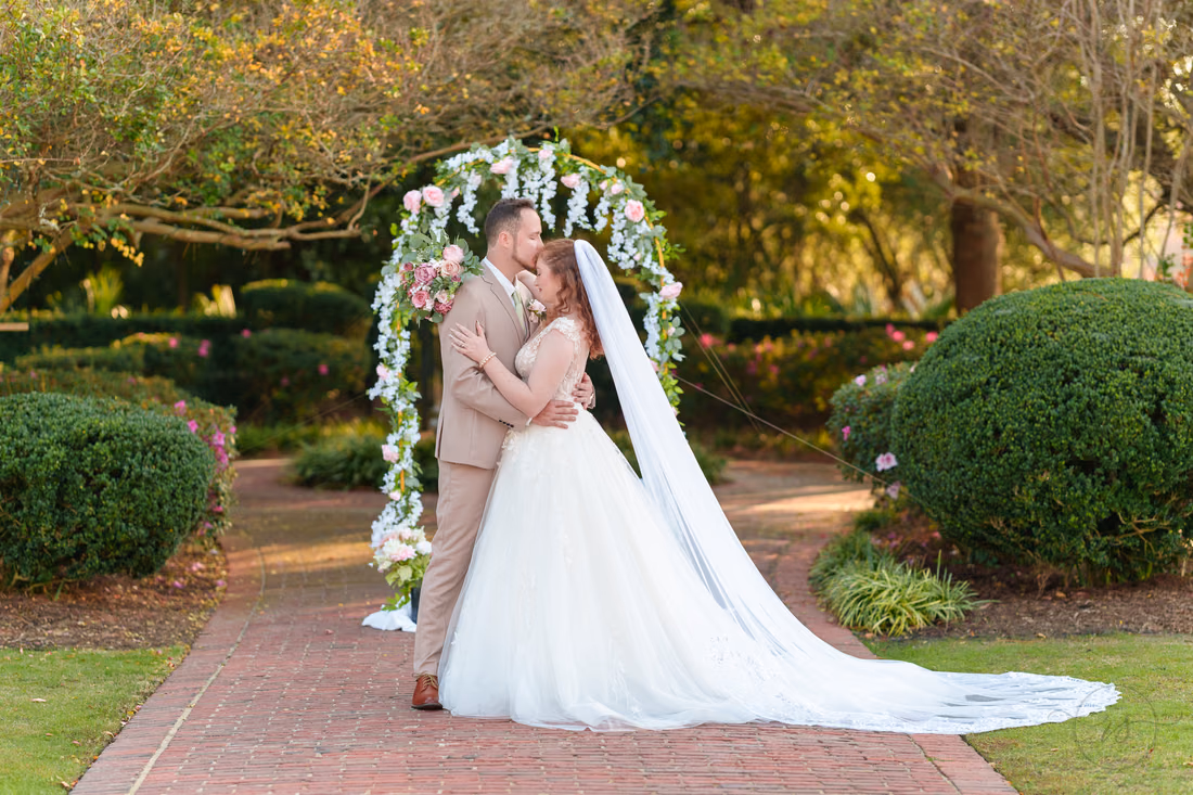 The bride and groom share a kiss under the flower arch at Pine Lakes Country Club
