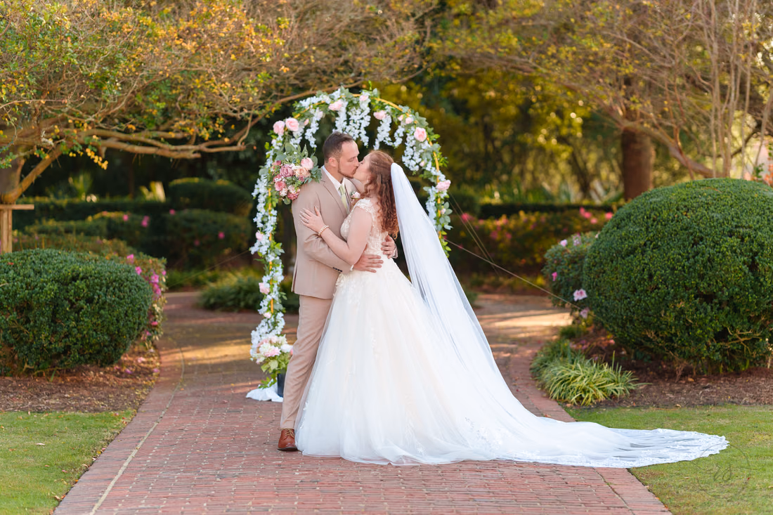 The bride and groom kiss with her veil trailing down the brick path at Pine Lakes Country Club