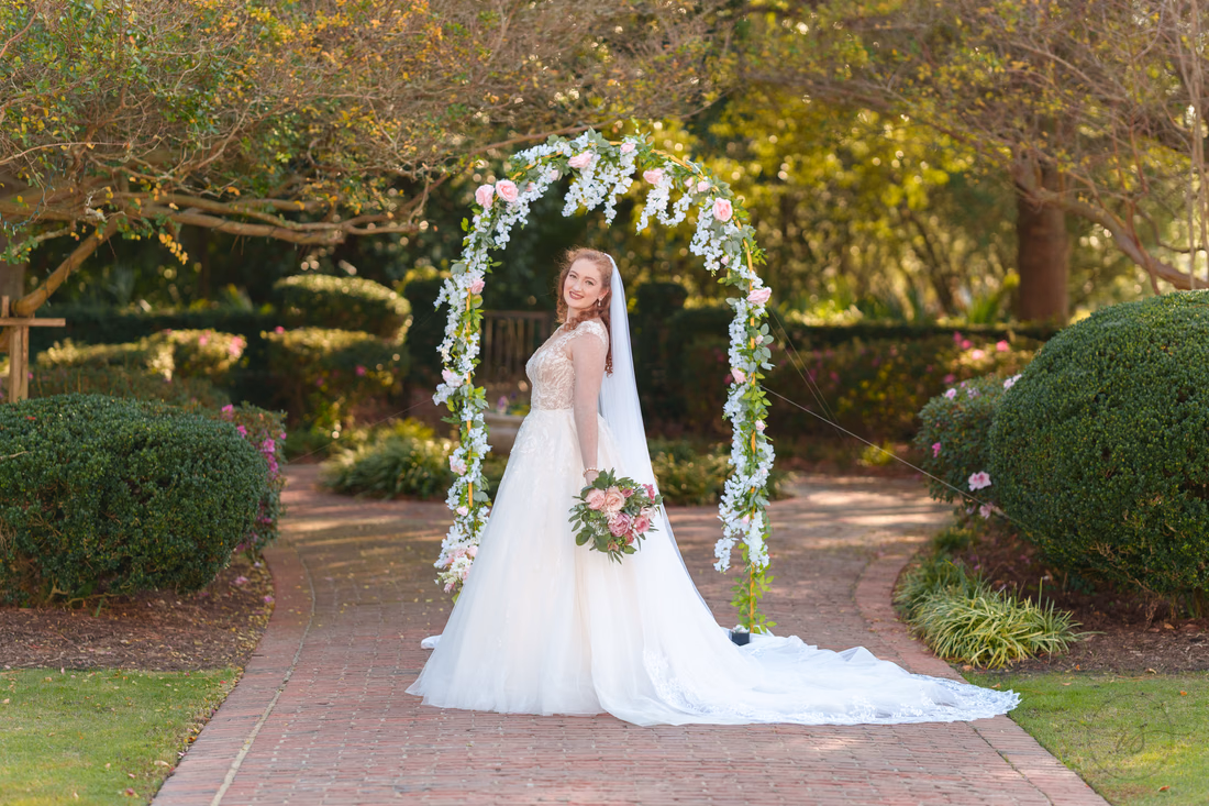 The bride poses with her bouquet in front of the flower arch at Pine Lakes Country Club