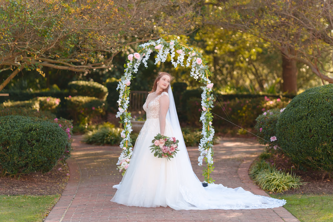 The bride looks over her shoulder by the flower arch in the garden at Pine Lakes Country Club
