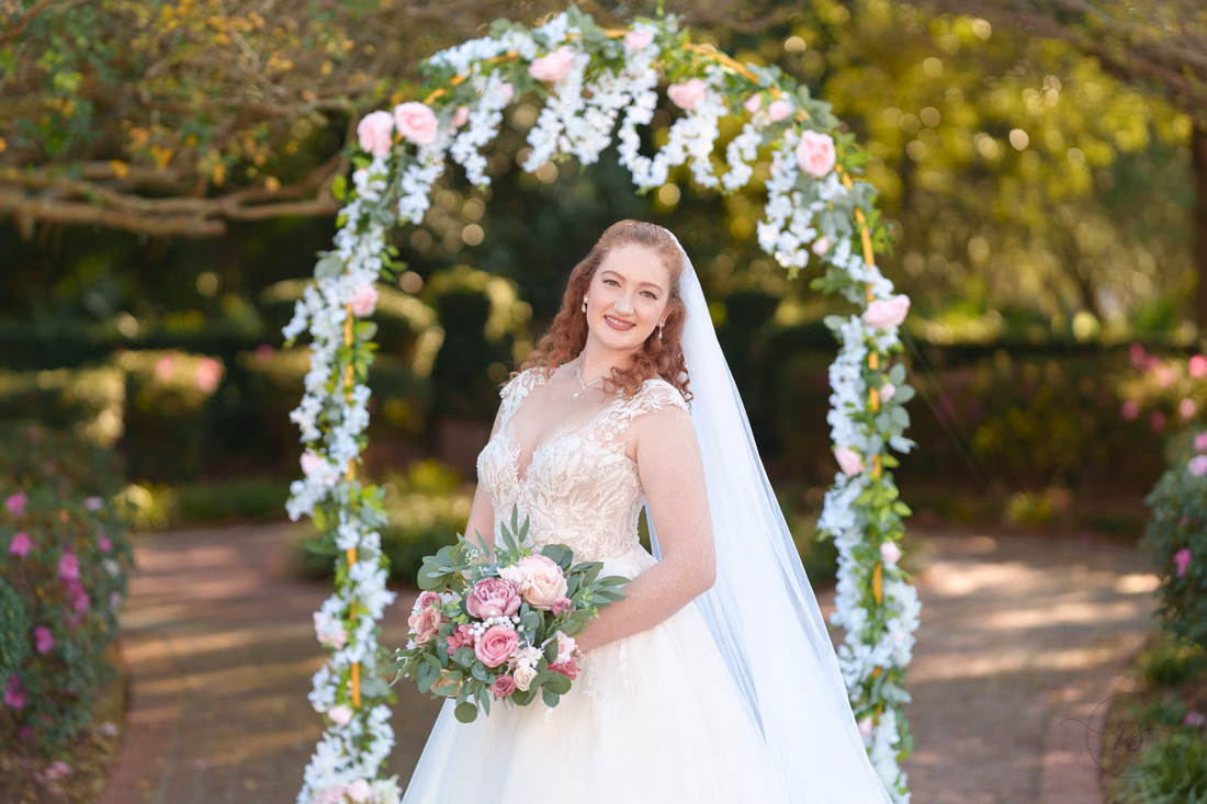 Close portrait of the bride smiling with her pink bouquet under the flower arch at Pine Lakes Country Club