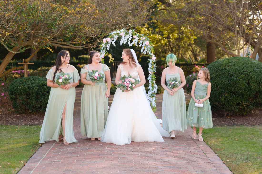 The bride laughs with her bridesmaids on the garden path at Pine Lakes Country Club