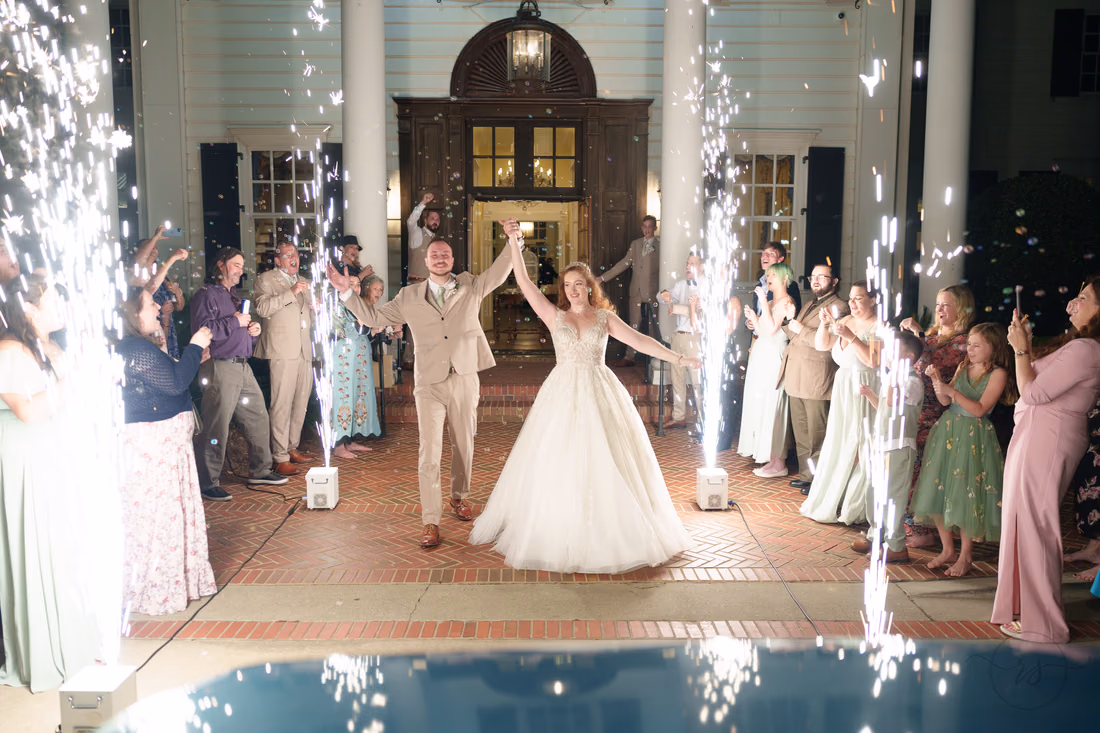 The bride and groom raise their hands between cold sparkler fountains at Pine Lakes Country Club