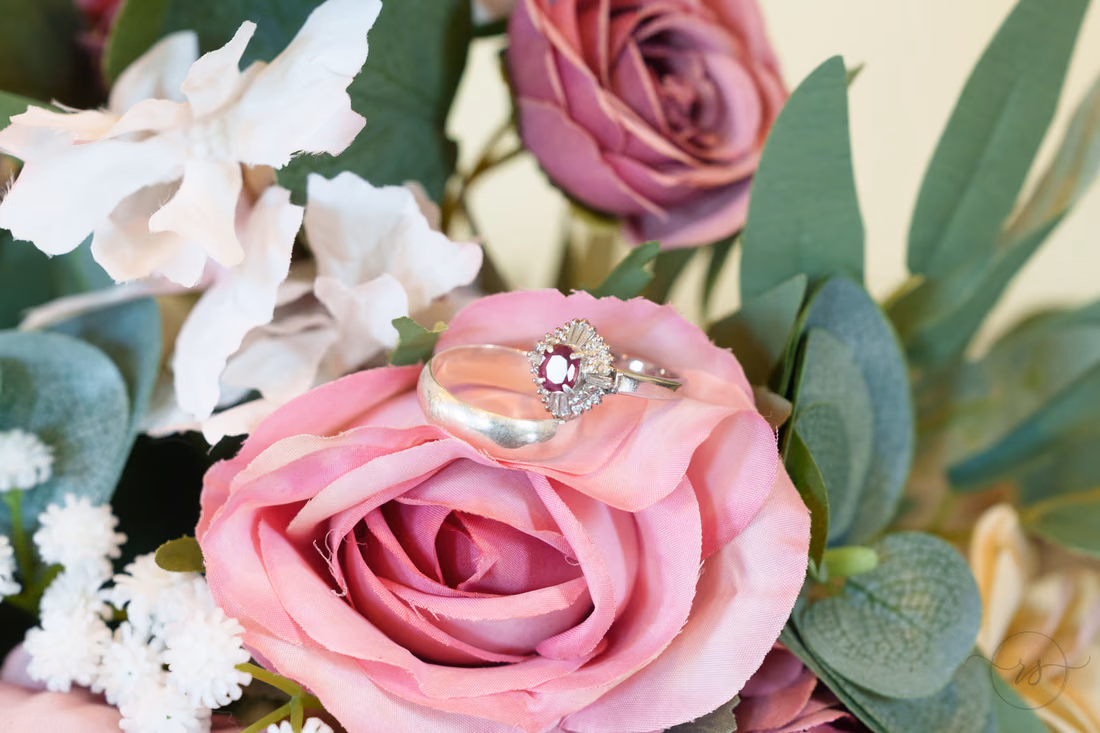 Wedding rings resting on a pink rose in the bouquet at Pine Lakes Country Club