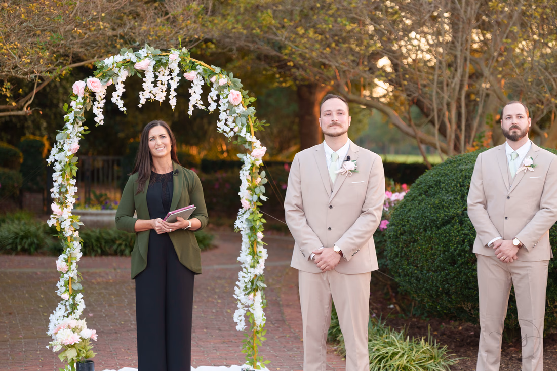The officiant, groom and best man wait under the flower arch at Pine Lakes Country Club