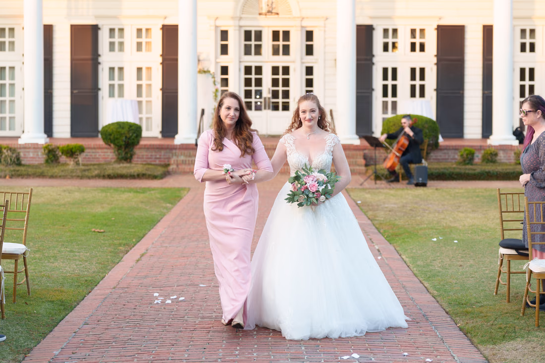 The bride smiles as she is escorted down the aisle past the cellist at Pine Lakes Country Club