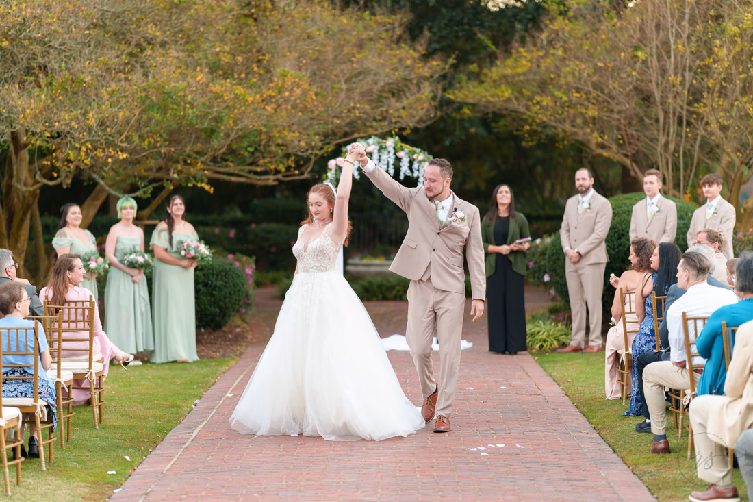 The groom raises the bride's hand in celebration after the ceremony at Pine Lakes Country Club