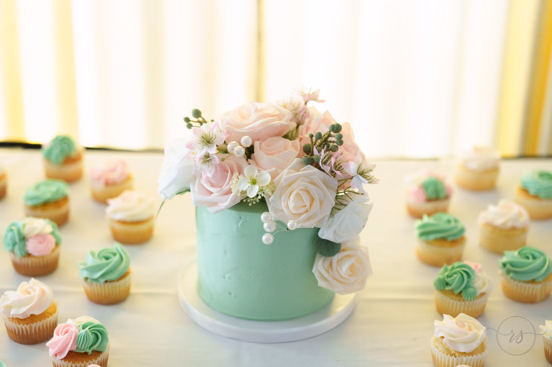 Mint green wedding cake topped with roses among cupcakes at Pine Lakes Country Club