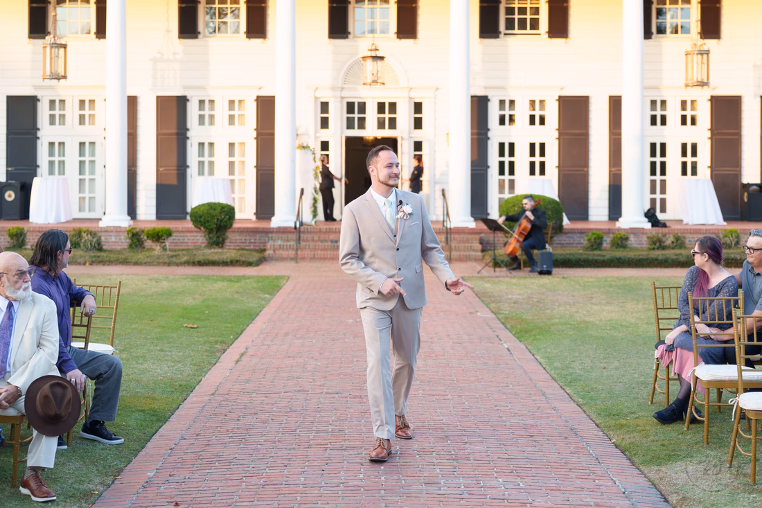 The groom walks down the brick aisle in front of the clubhouse at Pine Lakes Country Club