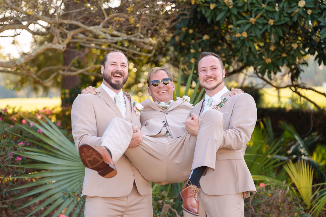 The groom and a groomsman carry a laughing groomsman in sunglasses at Pine Lakes Country Club