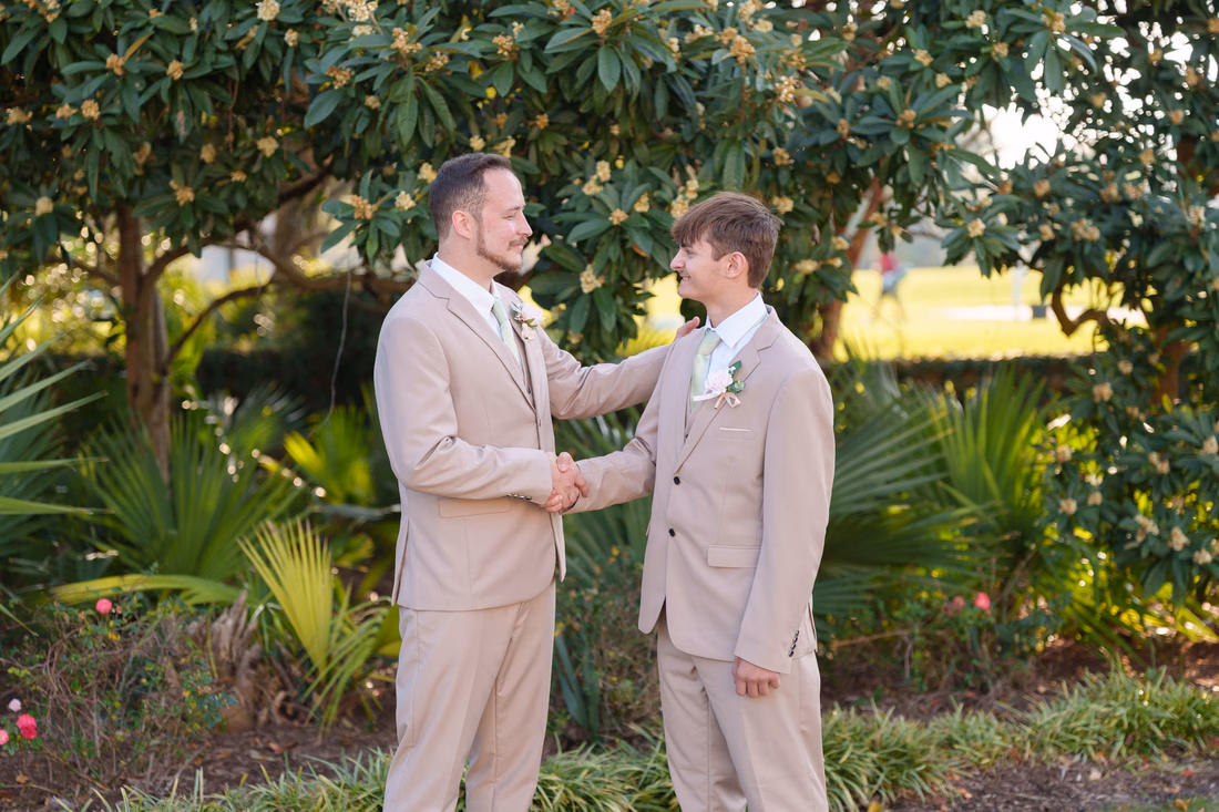 The groom shakes hands with a young groomsman in the garden at Pine Lakes Country Club
