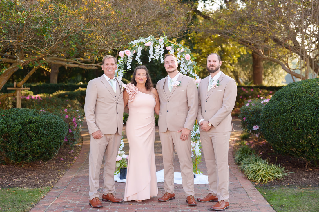 The groom with family members under the flower arch at Pine Lakes Country Club