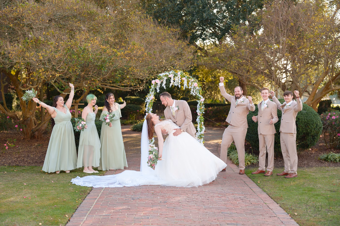 The groom dips the bride as the wedding party cheers at Pine Lakes Country Club
