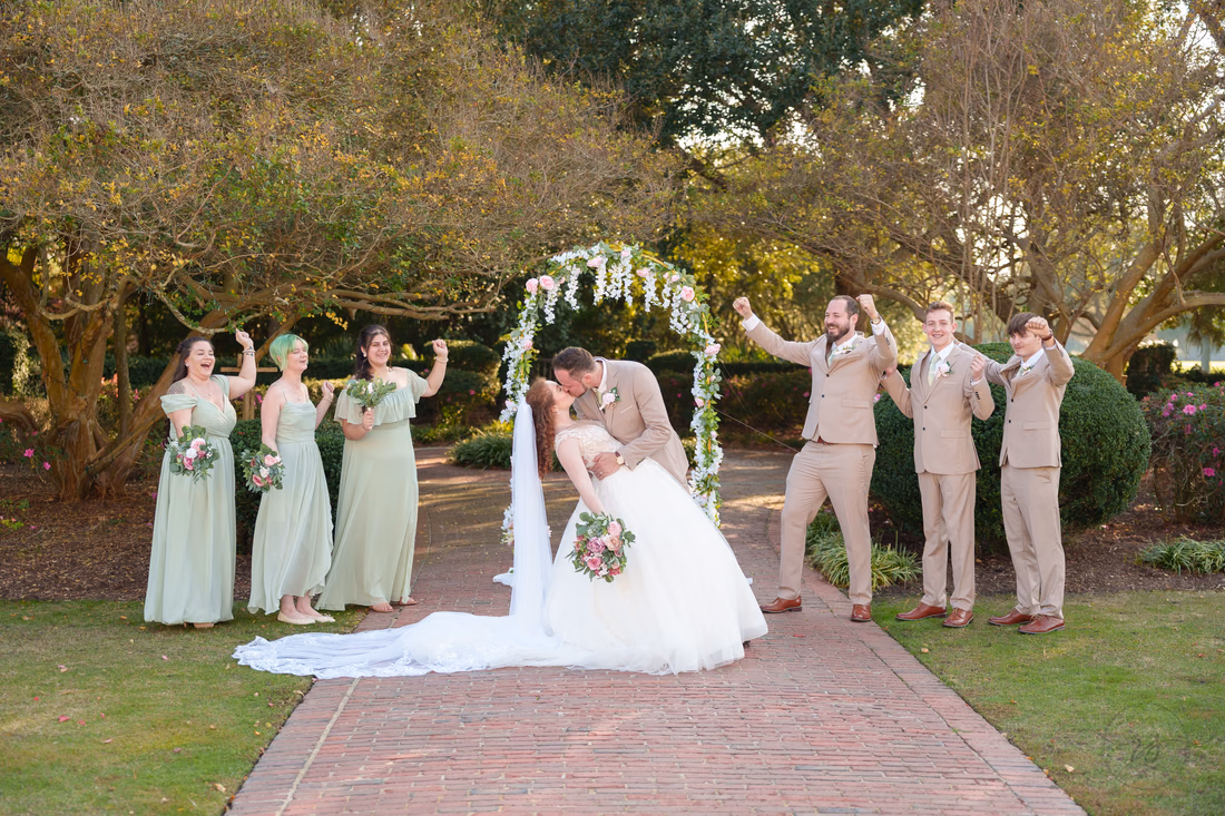 The groom dips the bride for a kiss in front of the cheering wedding party at Pine Lakes Country Club