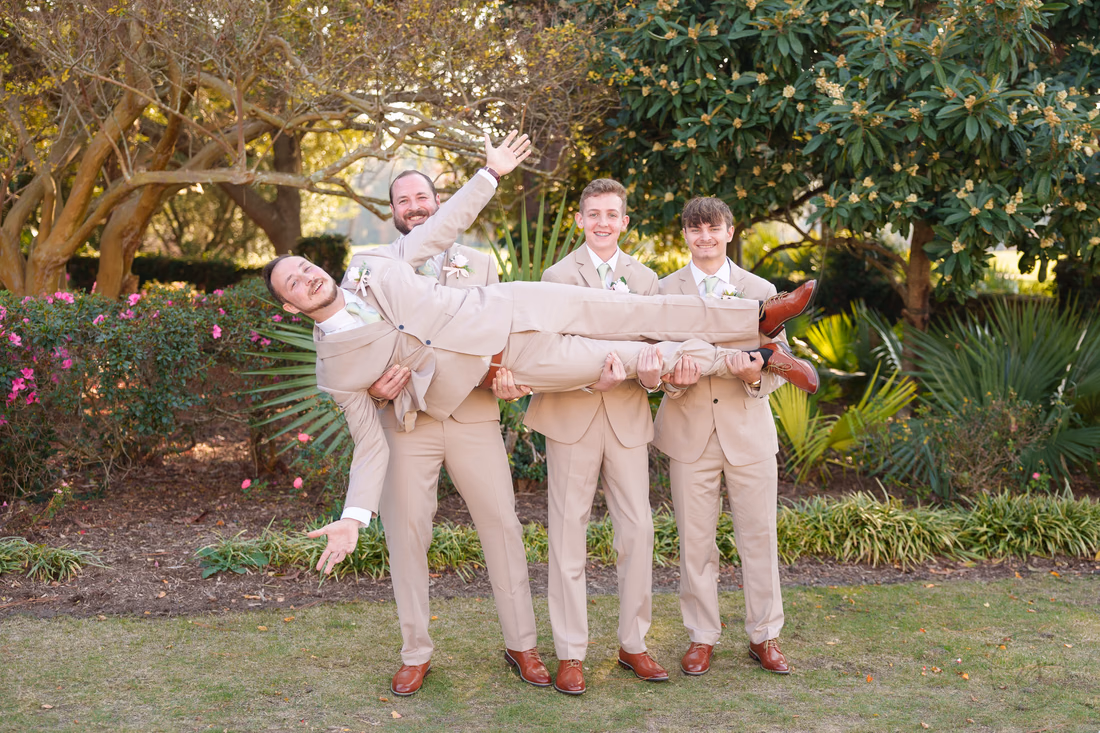 Groomsmen carry the groom sideways in the garden at Pine Lakes Country Club