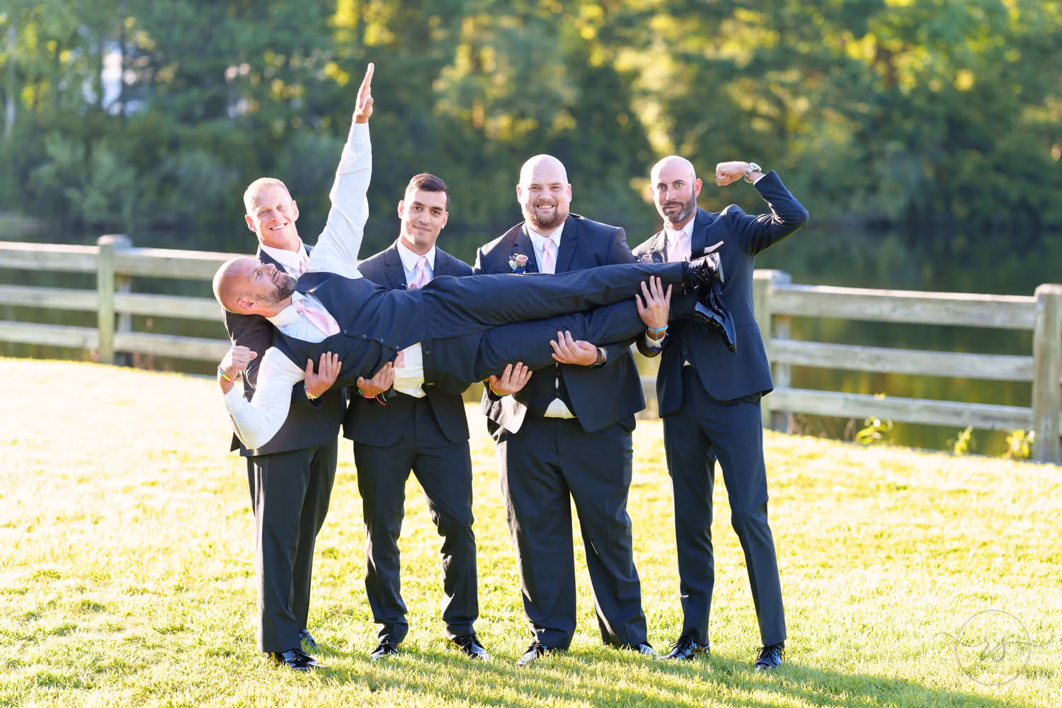 Groomsmen in navy suits flexing while holding the groom sideways in the air at The Pavilion at Pepper Plantation