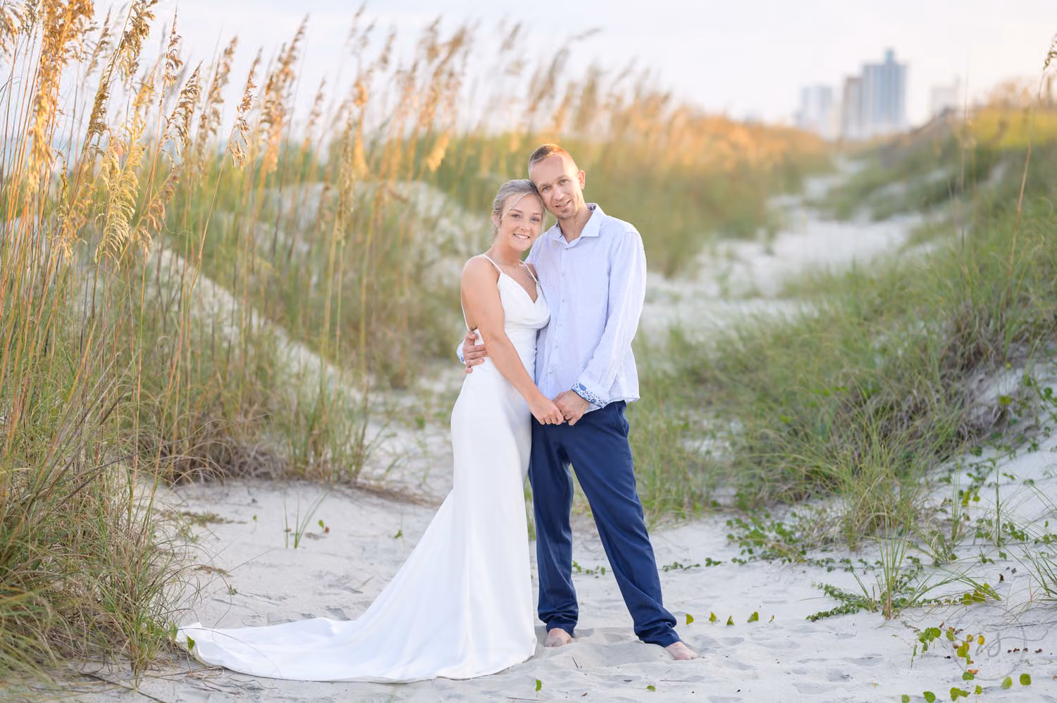 Bride and groom standing on a sandy path between sea oats and dunes on the beach in Myrtle Beach