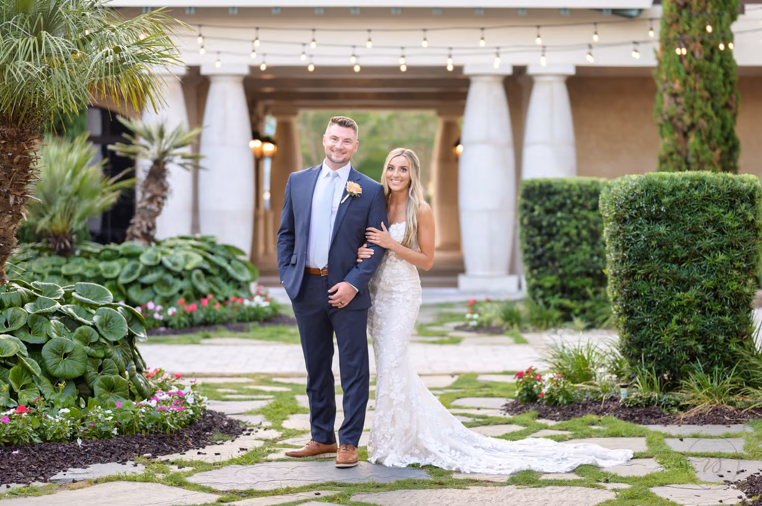 Bride and groom in a light gray suit standing arm in arm and smiling in the columned courtyard garden at 21 Main Events