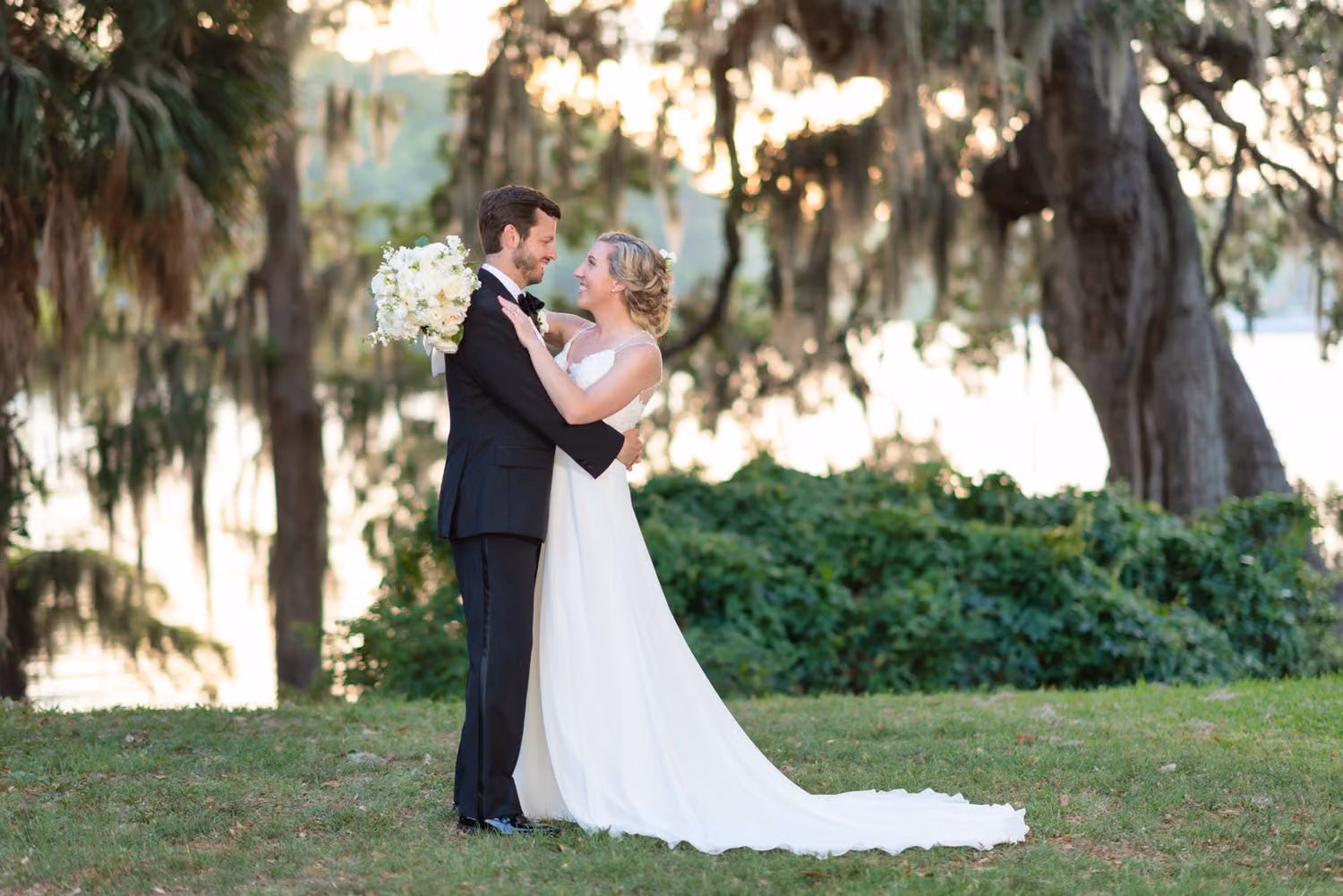 Groom holding the bride close under moss-draped trees beside the Waccamaw River at Wachesaw Plantation