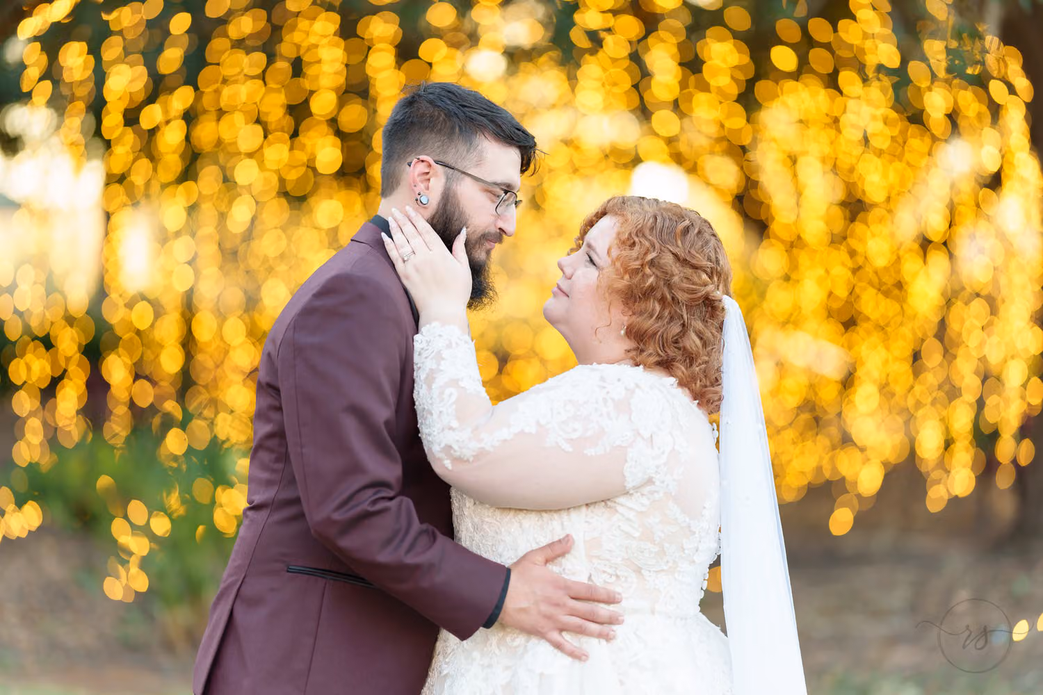 Groom in a burgundy jacket holding the bride close in front of glowing golden string lights at The Cypress Inn