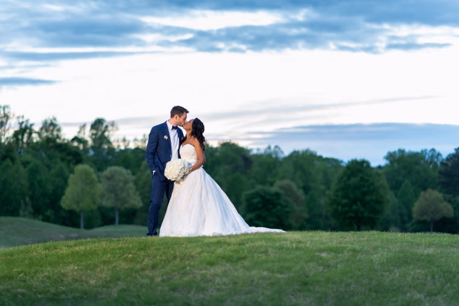 Bride and groom standing on a grassy golf course hill under a blue evening sky at River Ridge Golf Club