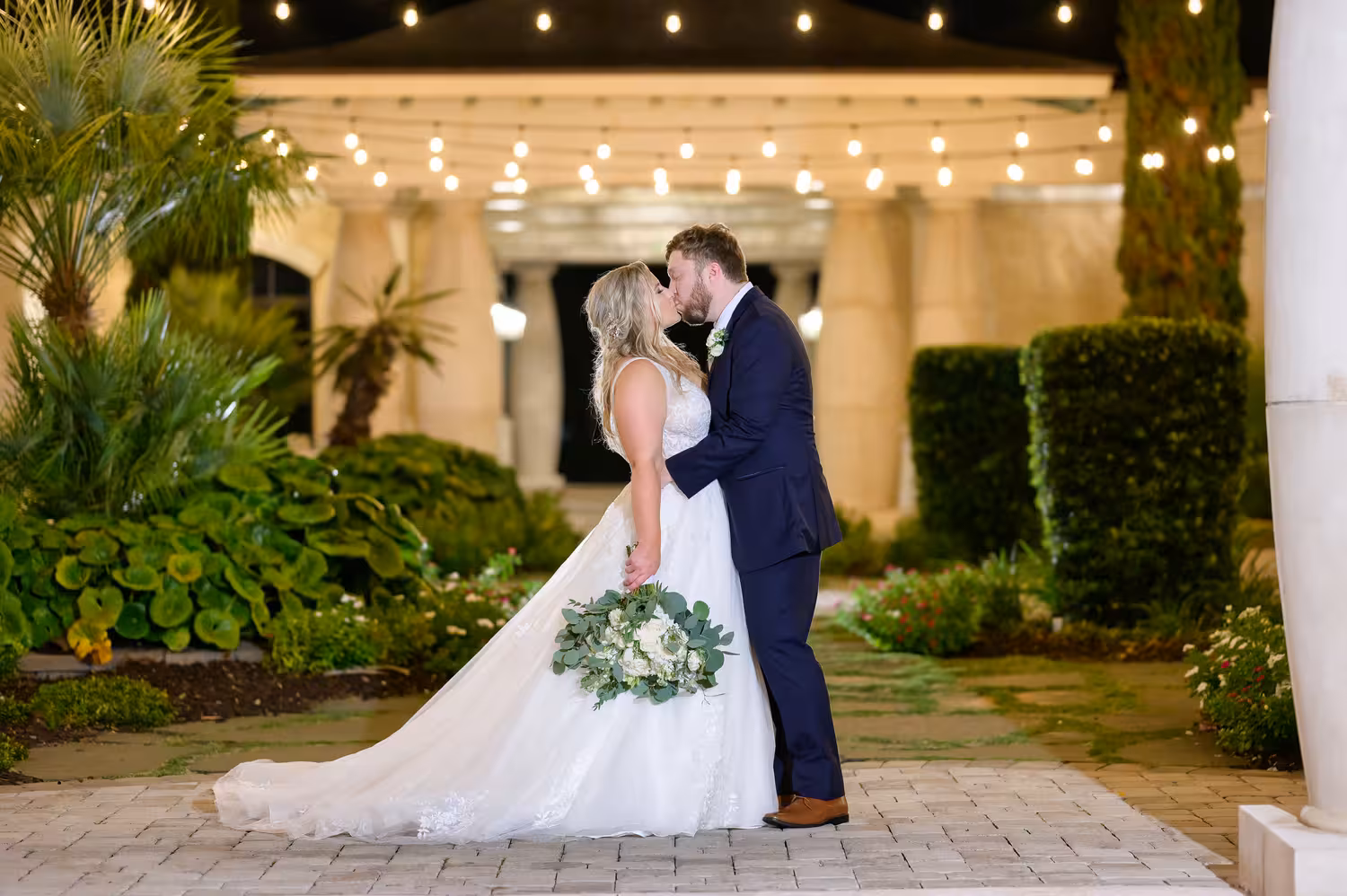 Bride and groom kissing in the courtyard under string lights at 21 Main Events