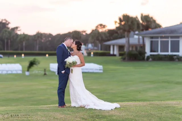 Bride and groom kissing on the hill behind the clubhouse at Dunes Golf and Beach Club