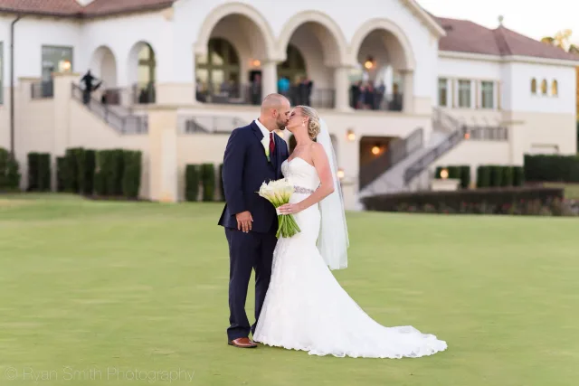 Bride and groom kissing on the lawn with the Grande Dunes Members Club behind them