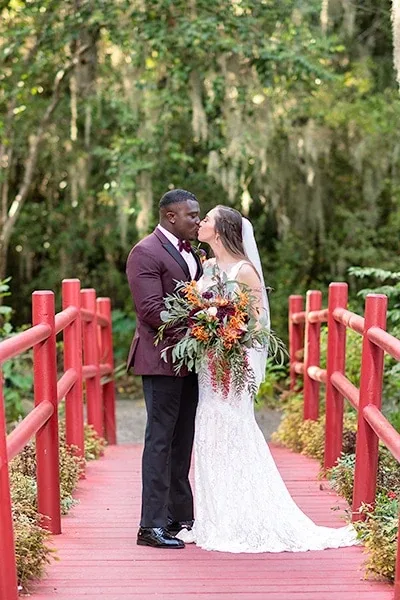 Bride and groom kissing on a red wooden bridge at Magnolia Plantation in Charleston