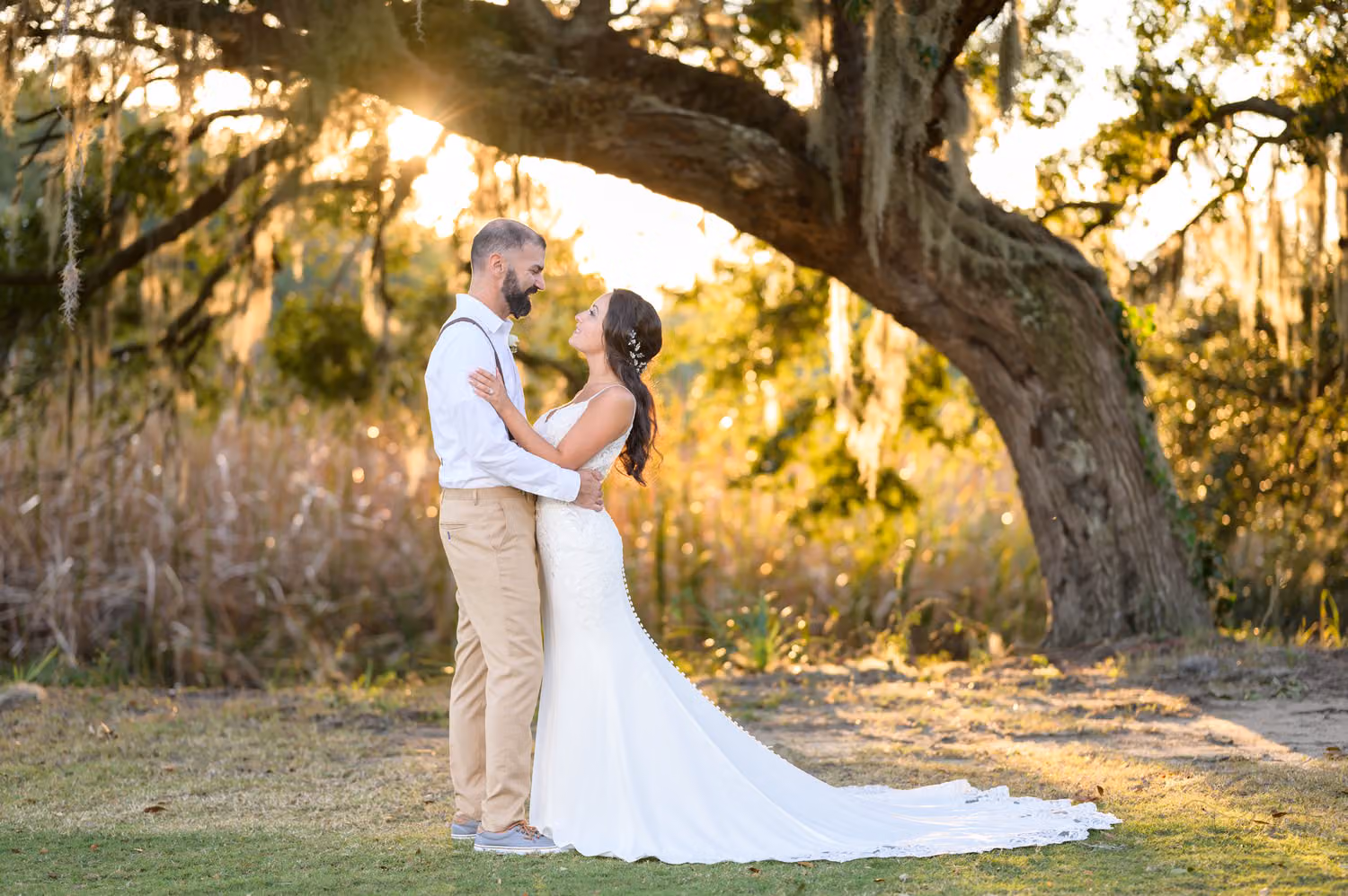 Bride and groom holding each other as the sun sets behind a sprawling live oak at Pawleys Plantation Golf & Country Club