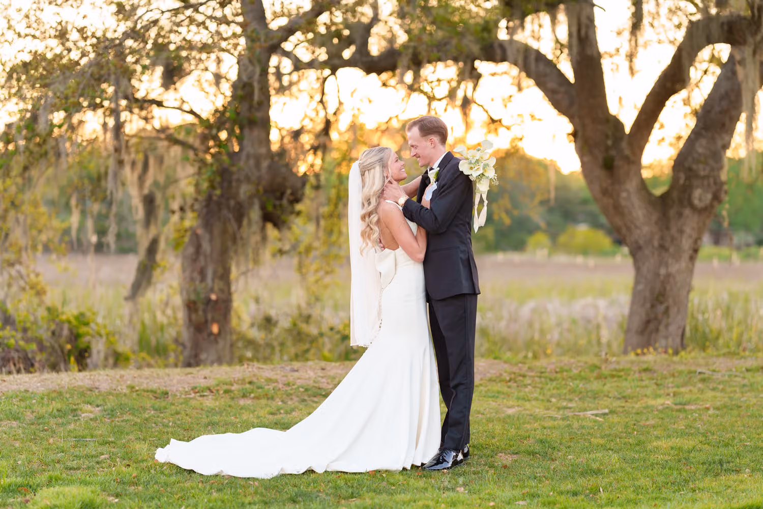 Bride and groom kissing in sunset light with oaks and the marsh behind them at Pawleys Plantation
