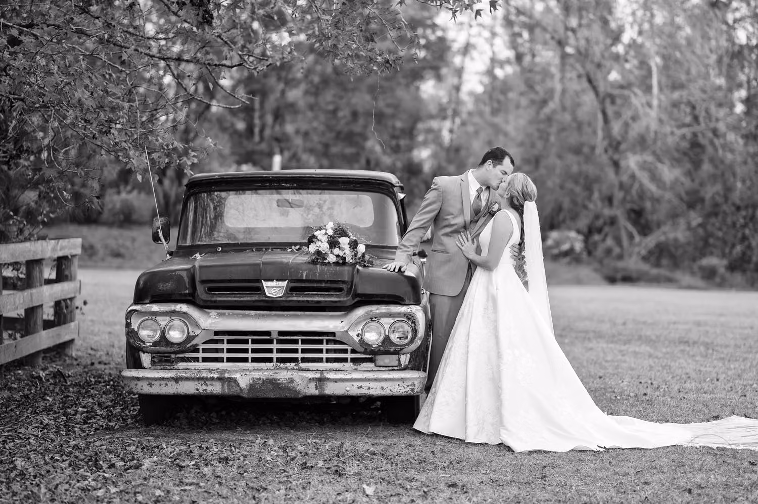 Black and white portrait of the bride and groom kissing beside an old pickup truck at The Blessed Barn