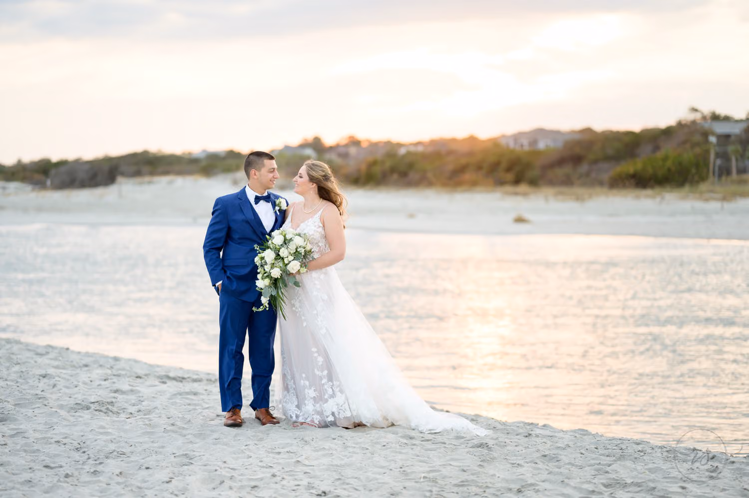 Bride and groom in a navy suit standing on the sandy shore of the inlet at sunset at 21 Main Events at North Beach