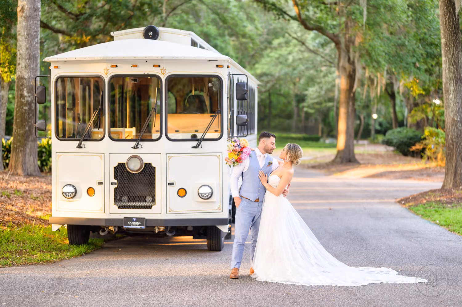 Bride and groom kissing on the drive beside a vintage white trolley under the oaks at Pawleys Plantation Golf & Country Club