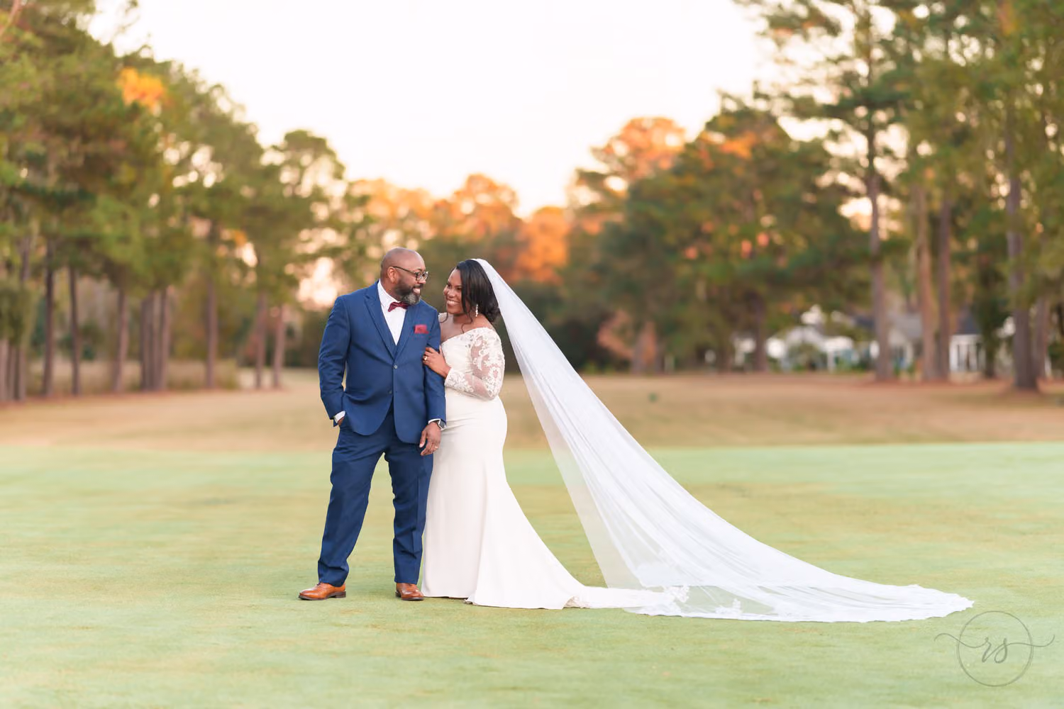 Bride with a long veil holding the groom's arm and looking up at him on the green at Wedgefield Country Club