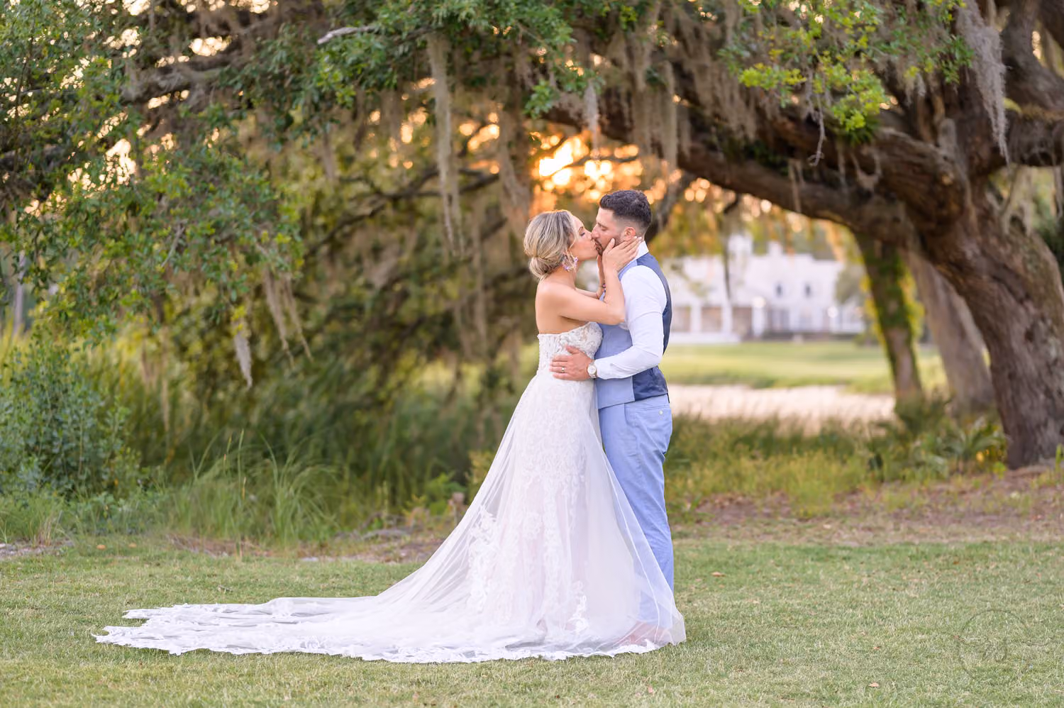 Bride pulling the groom in for a kiss under mossy oaks in sunset light at Pawleys Plantation Golf & Country Club