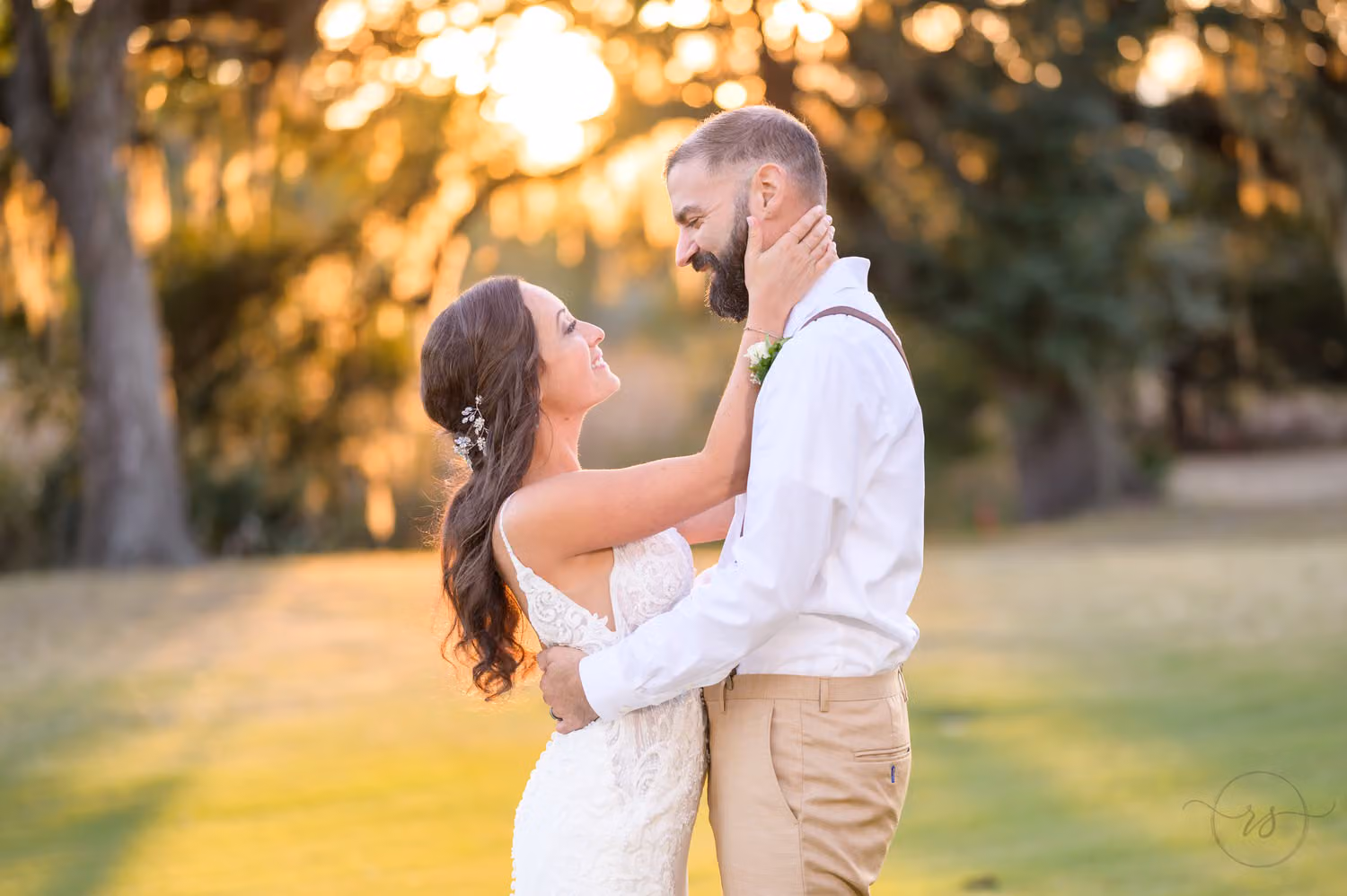Bride holding the groom's face as the sun sets through the trees behind them at Pawleys Plantation Golf & Country Club
