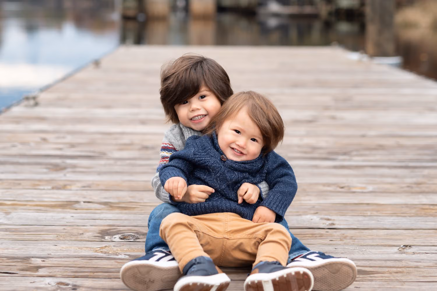 Older brother hugging his little brother as they sit together on a wooden dock at the Conway Riverwalk