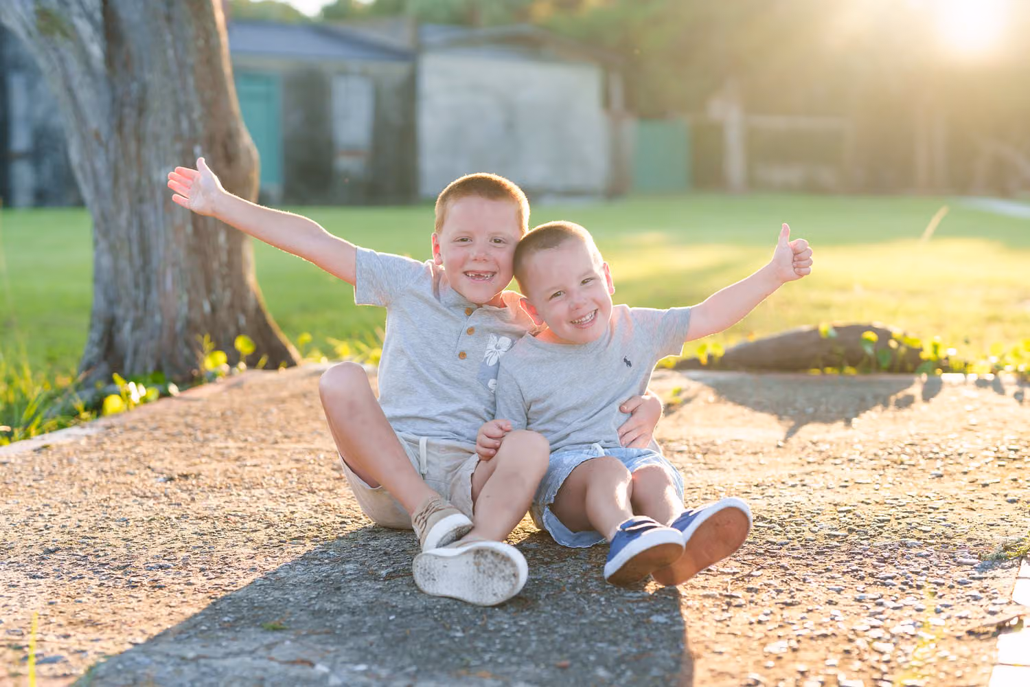 Two little brothers sitting on a log in the park with their arms thrown wide at sunset at Huntington Beach State Park