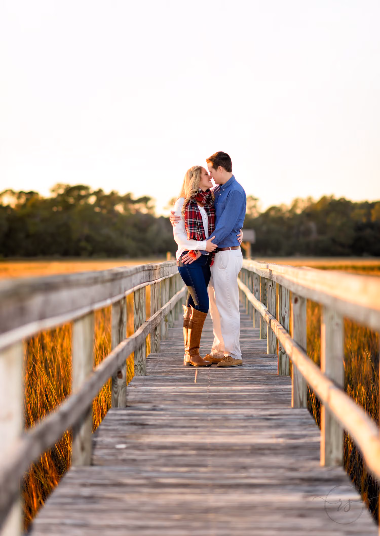 Couple kissing at the end of a long wooden walkway over the marsh in evening light in Murrells Inlet