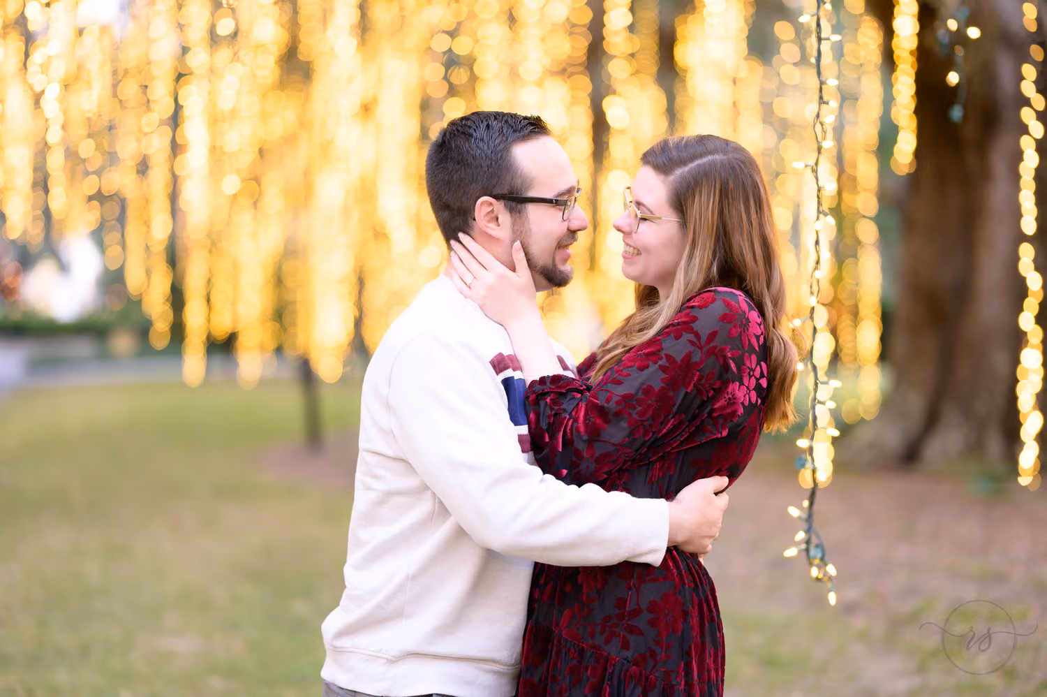 Couple in winter clothes holding each other close in front of curtains of warm hanging lights at Brookgreen Gardens