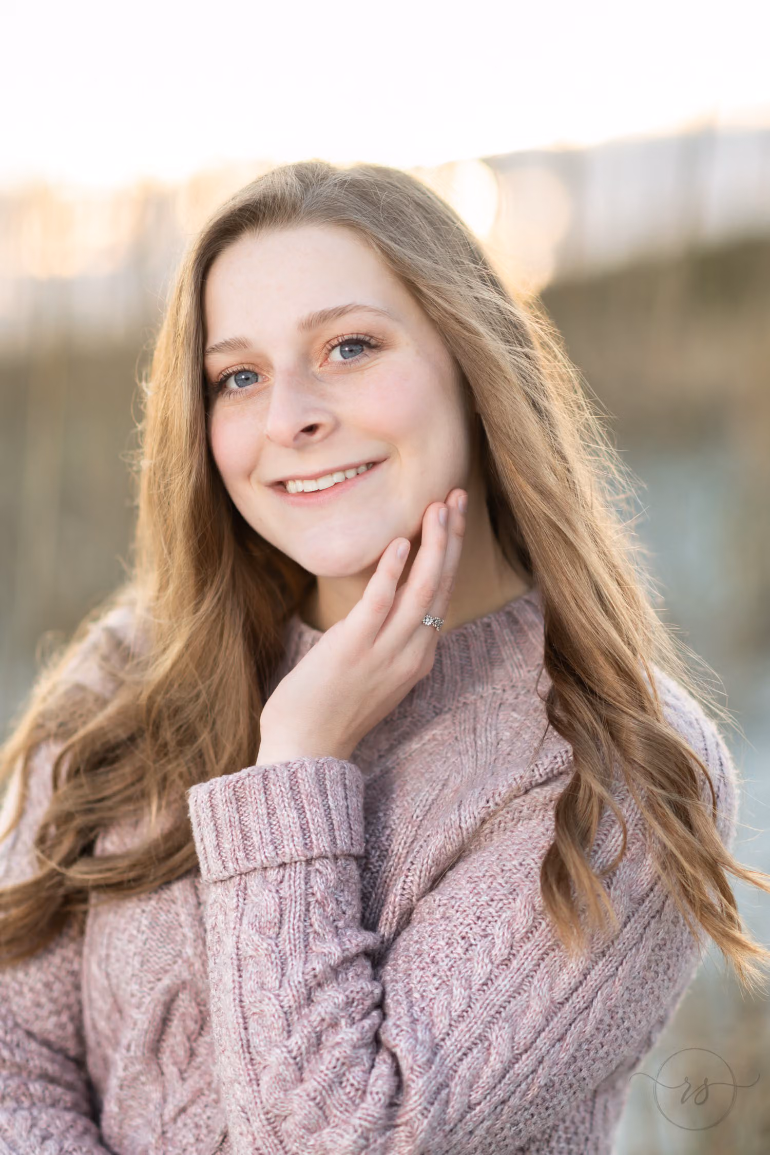 Close-up of a smiling senior with long hair and her hand at her chin by the sea oats at Huntington Beach State Park