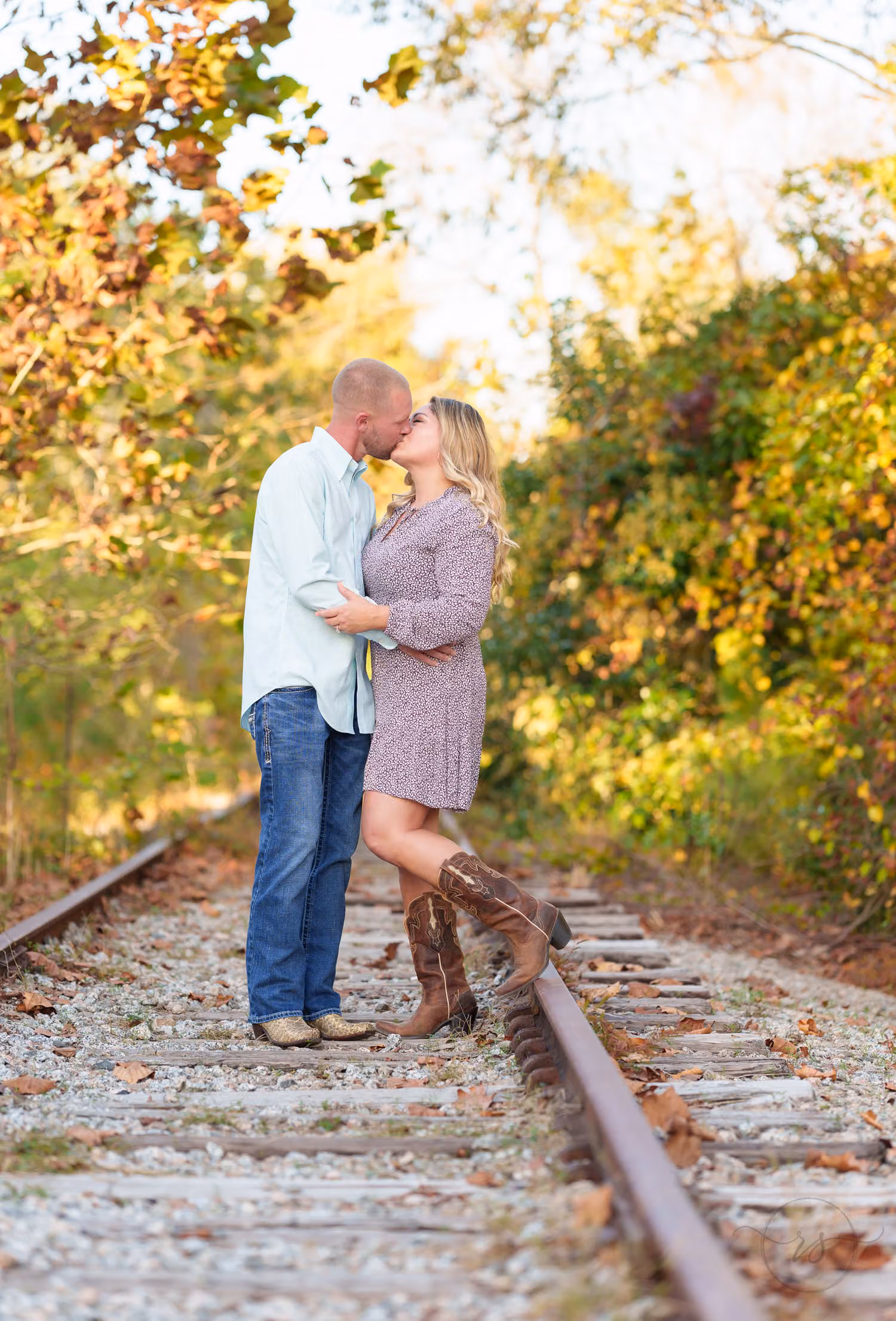 Couple in cowboy boots kissing as she kicks up a heel on the old train tracks at the Conway Riverwalk
