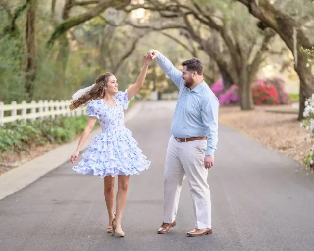 Couple dancing as he spins her down an oak-lined road with pink azaleas at Caledonia Golf and Fish Club