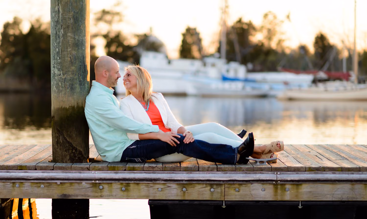 Couple relaxing on a wooden dock beside a piling with boats in the harbor behind them in Downtown Georgetown