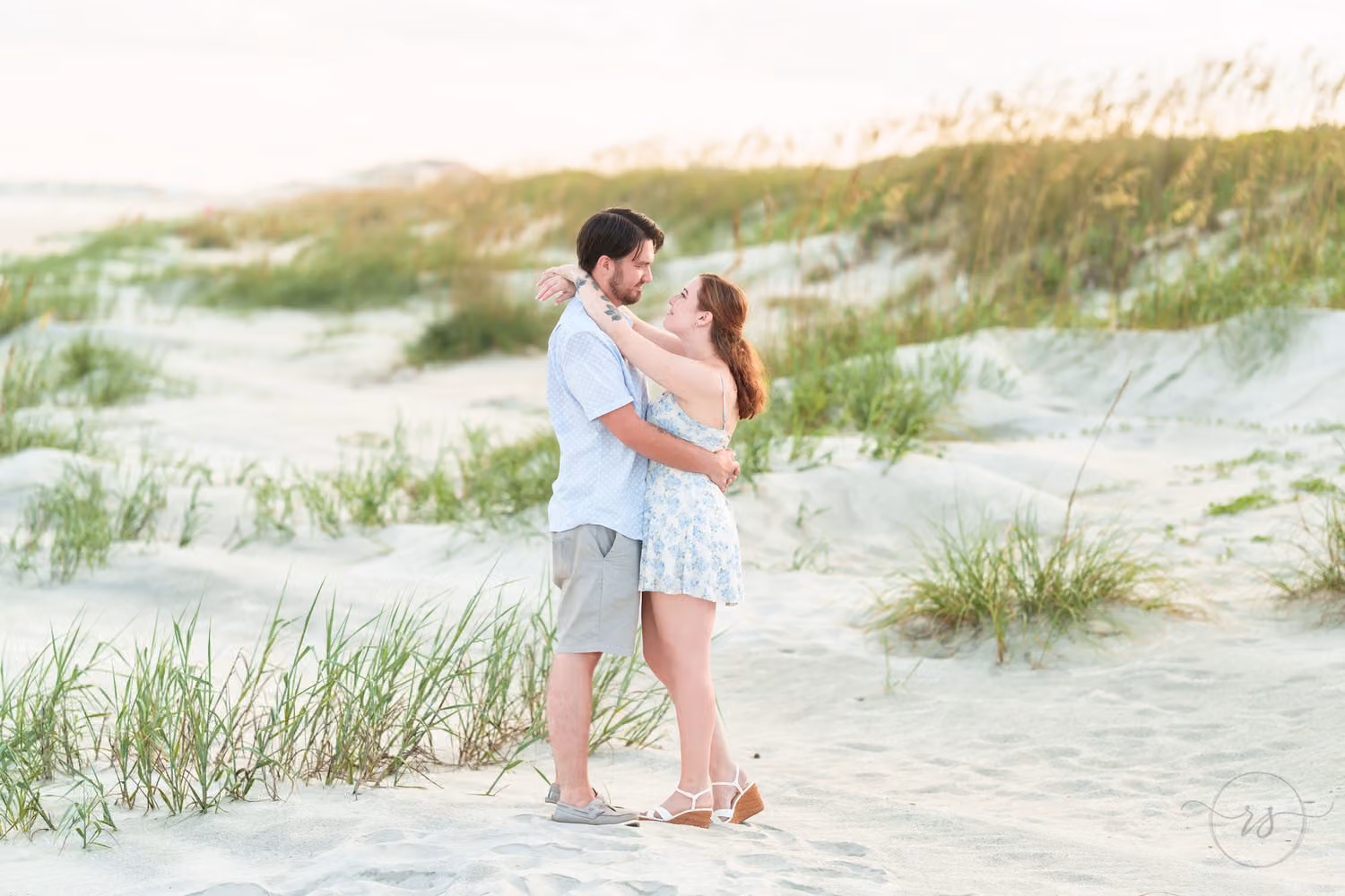 Couple hugging in the white sand between clumps of sea oats on the dunes at Huntington Beach State Park