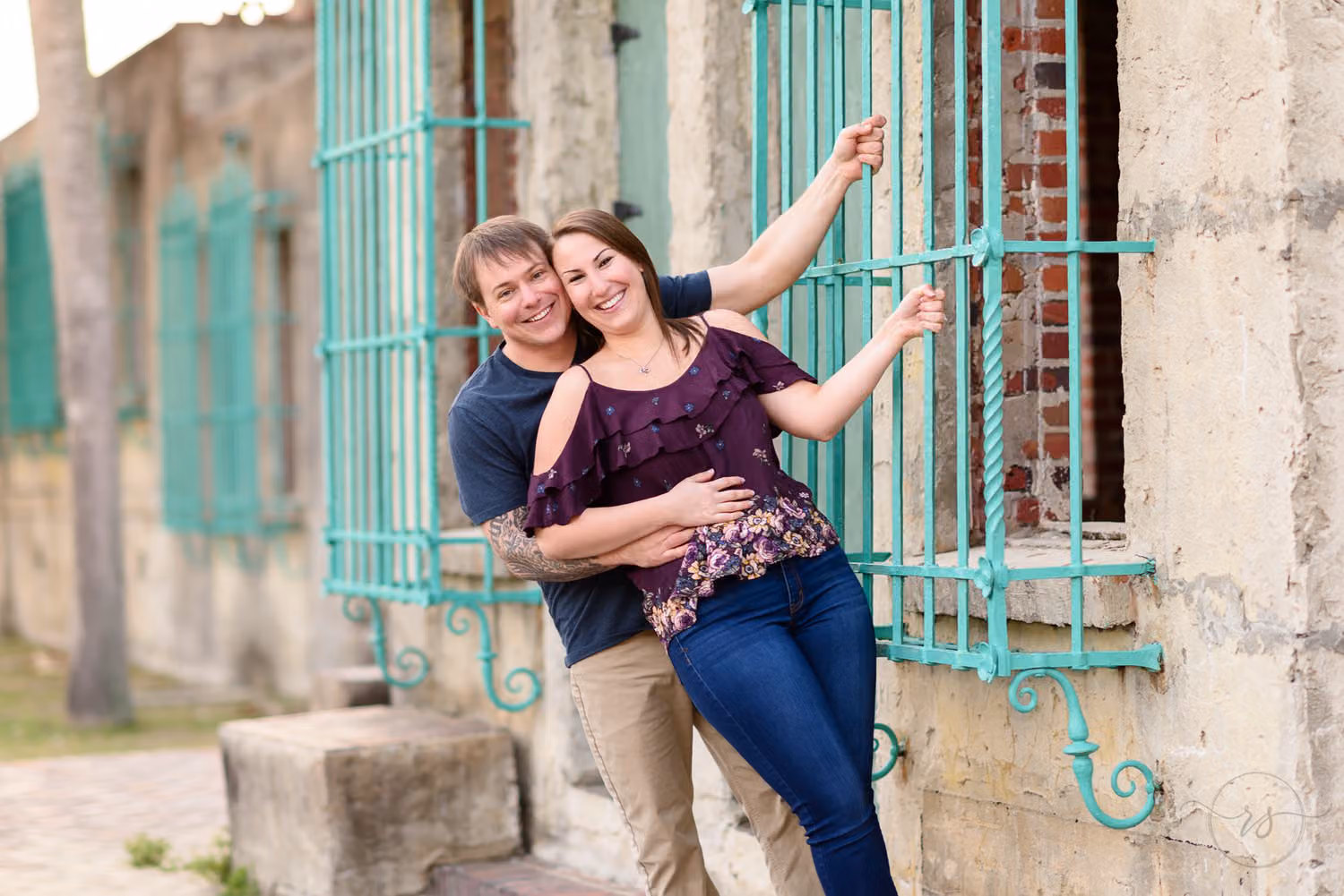 Smiling couple posing playfully by the teal window grates on the stone walls of the Atalaya Castle