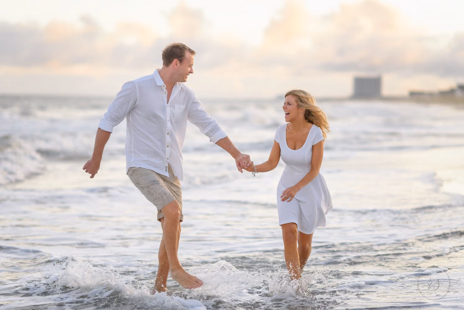 Couple holding hands and splashing through the shallow waves under a cloudy sky at Myrtle Beach State Park